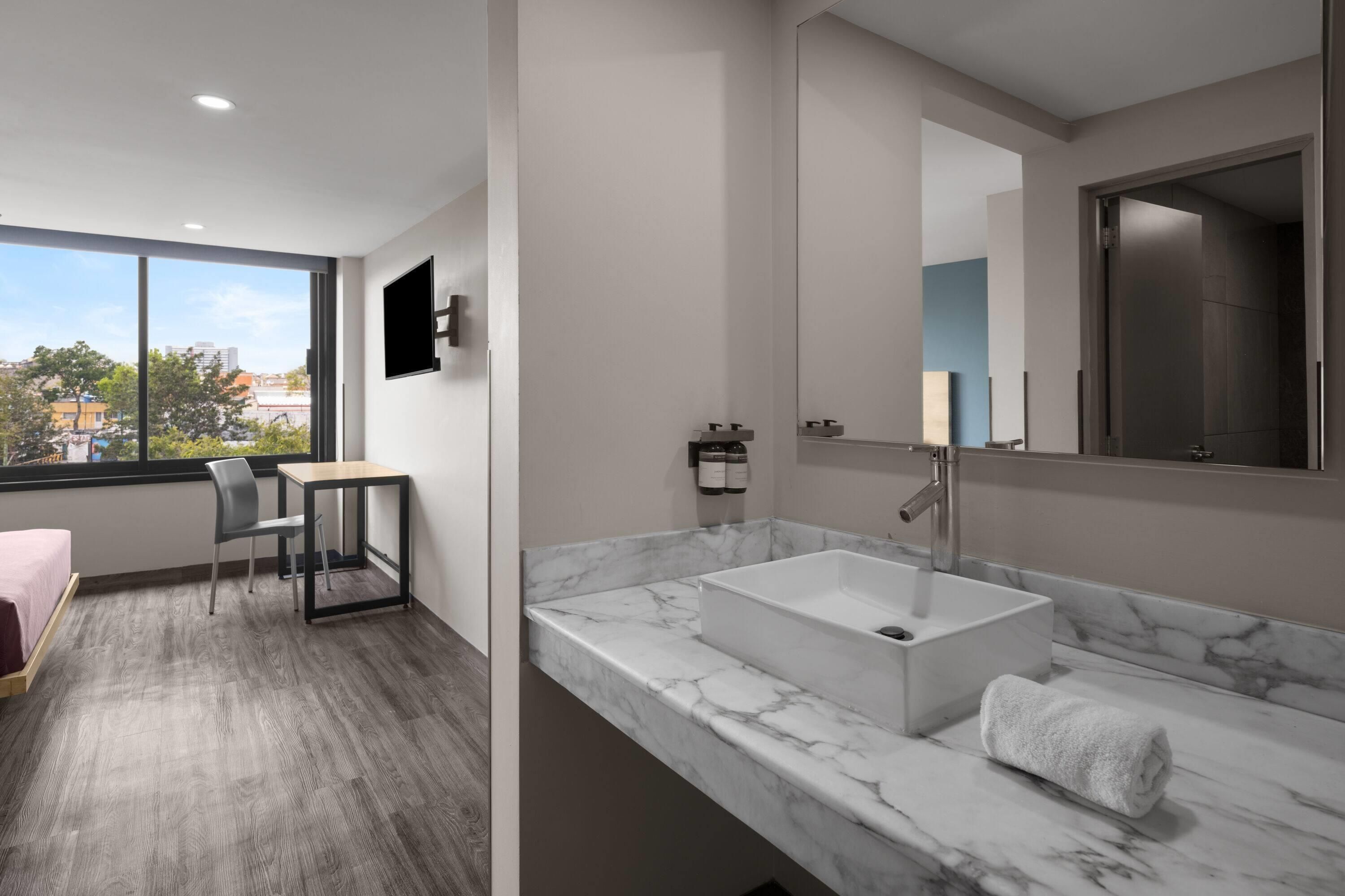 A modern bathroom with a large window, a marble sink, and a chair.