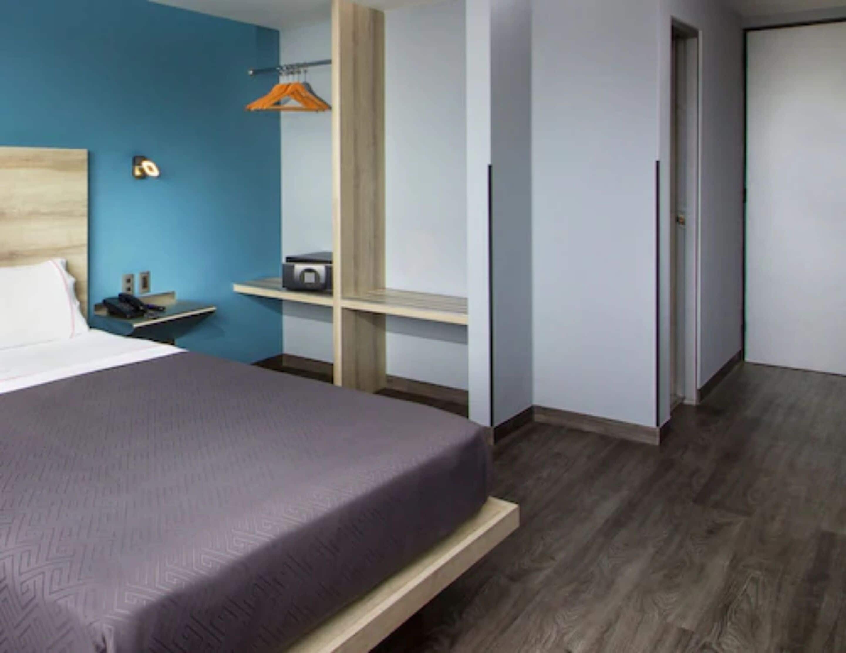 Ein modernes Hotelzimmer mit einem Bett, einem Schreibtisch mit Telefon und einem kleinen Regal mit Radio.