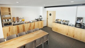 A modern breakfast area with a long wooden table and chairs, a buffet counter with various food options, and a coffee machine. - Hotel MX lagunilla CDMX, Trademark Collection by Wyndham (Mexico City)
