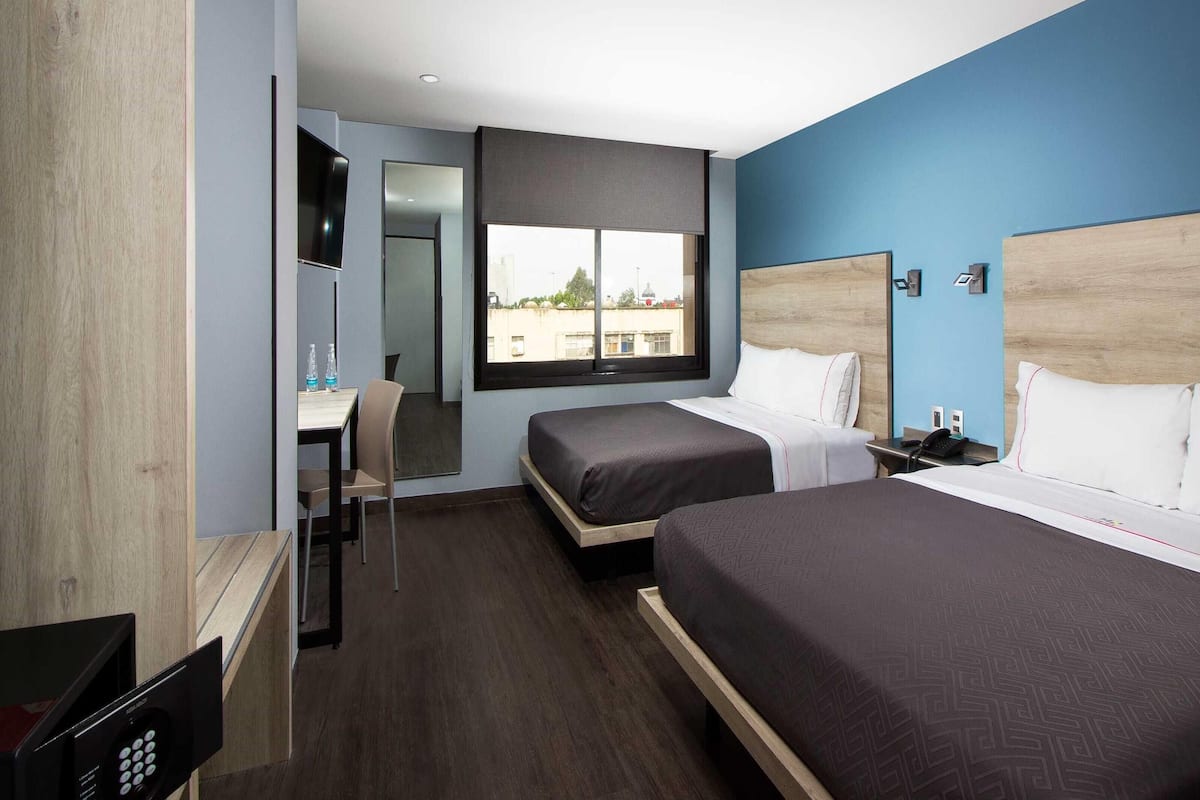 Een hotelkamer met twee bedden, een bureau, een stoel, een televisie en een raam met uitzicht op de stad.