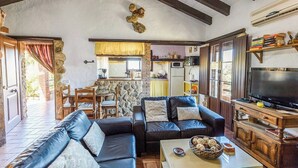 A living room with a sofa, TV, and a kitchen in the background. - Jara de El Gastor by Ruralidays (Cádiz)