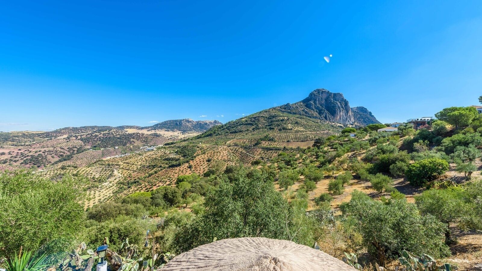 Un paisaje montañoso con un pico destacado, vegetación dispersa y un cielo azul despejado.