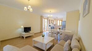 A living room with a sofa, coffee table, TV, and dining area with chairs and a table.