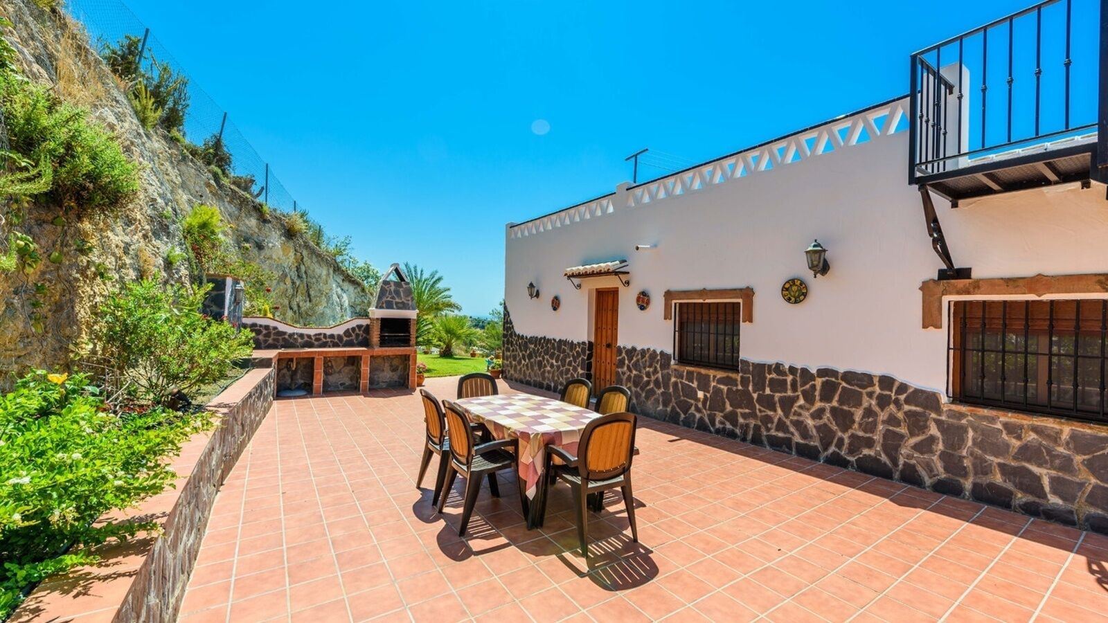 An outdoor patio with a stone wall, a dining table with chairs, and a stone oven.