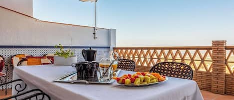 A terrace with a table set for breakfast, including fruits, a coffee pot, and a glass pitcher.