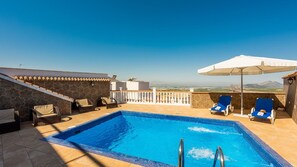 A rooftop pool with blue tiles, surrounded by lounge chairs and an umbrella.