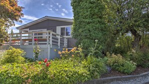 A modern house with a balcony, surrounded by lush greenery and flowering plants. - Cute Cottage w/ Deck Walk 115 Ft to Brewery & Cafe (Poulsbo)