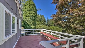 A wooden deck with a white railing, a red bench, and a view of trees and a building. - Cute Cottage w/ Deck Walk 115 Ft to Brewery & Cafe (Poulsbo)