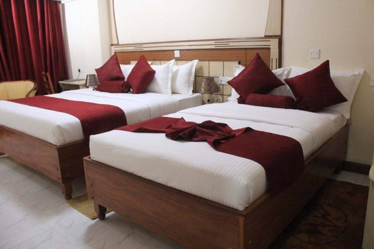 Een hotelkamer met twee houten bedden, elk voorzien van witte lakens en rode sierkussens.