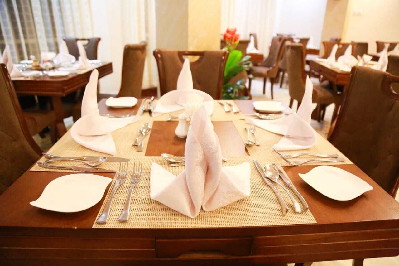 Een eetgedeelte met gedekte tafels, inclusief gevouwen servetten, bestek en borden.