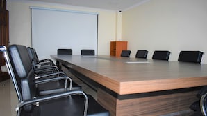 A conference room with a long table, six black chairs, a podium, and a projection screen.