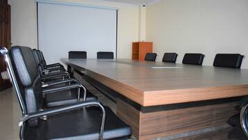 A conference room with a long table, six black chairs, a podium, and a projection screen.