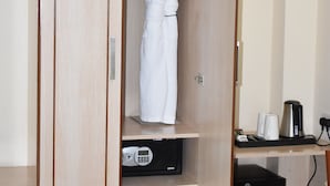 A wooden wardrobe with a robe hanging inside, a coffee maker, and a pair of slippers on the floor.