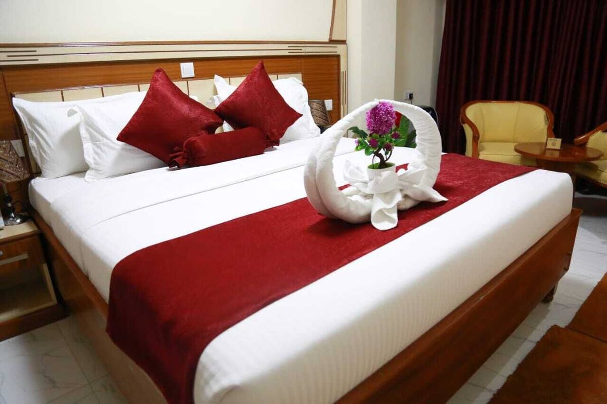 Een hotelkamer met een opgemaakt bed, een rode plaid en een decoratieve handdoek met een paarse bloem.