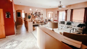 A spacious living room with a sofa, coffee table, and a dining area. There is a ceiling fan and a large window with curtains. - Welcome to Casa Lana !! (Gold Canyon)