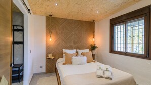 Quarto com cama, cabeceira de madeira, janela e mesa de cabeceira com abajur.