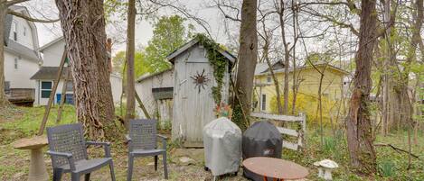 A backyard with a wooden shed, two covered chairs, a covered grill, and a small table.