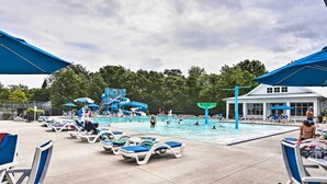 Un espace piscine avec des chaises longues, un toboggan aquatique et un bâtiment en arrière-plan.