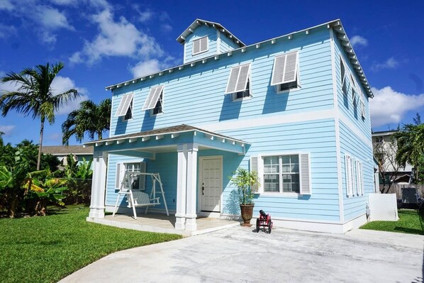 A two-story house with a porch, a swing set, and a wheelchair.