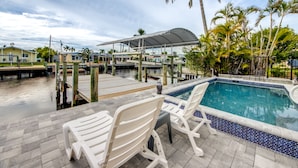 A pool area with white chairs, a covered seating area, and a view of the water and surrounding buildings. - Tropical Oasis Pool Kayak Bikes fish from dock  (Matlacha)