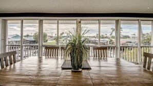 A spacious dining area with a large wooden table, a potted plant, and a view of the surrounding neighborhood through large windows. - Tropical Oasis Pool Kayak Bikes fish from dock  (Matlacha)