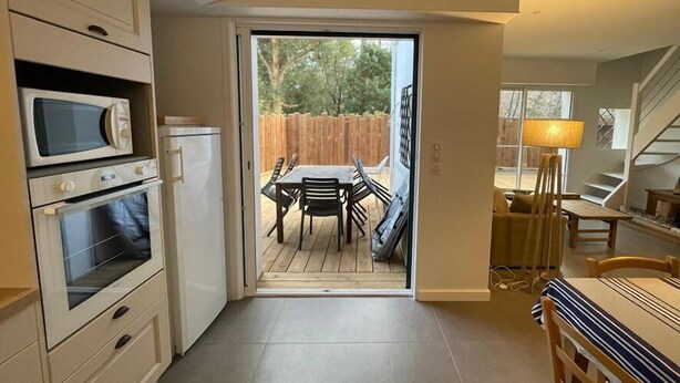 Une cuisine compacte dotée d’appareils électroménagers intégrés, un coin repas avec une table et des chaises, et une vue sur le jardin à travers une porte coulissante.