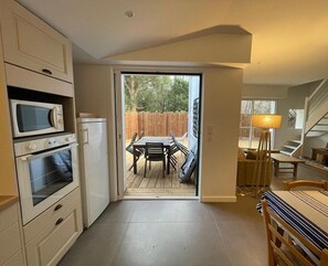 Cocina compacta con electrodomésticos integrados, comedor con mesa y sillas, y vista al patio trasero por una puerta corredera.