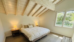 Une chambre avec un plafond en bois, un grand lit, des lampes de chevet, une table en bois et une fenêtre donnant sur un paysage verdoyant.