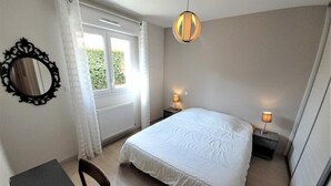 Une chambre à coucher avec un grand lit, deux tables de chevet avec des lampes, une chaise, une fenêtre avec des rideaux et un luminaire suspendu.