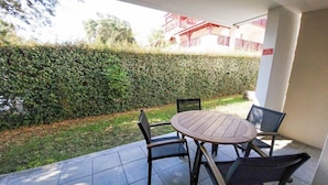 Un espace patio avec une table ronde et quatre chaises, entouré d’une haie basse et doté d’un sol carrelé.
