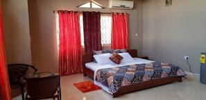 A bedroom with a bed, a chair, a small table, and a window with curtains.