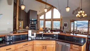 A kitchen with wooden cabinets, a stainless steel sink, and a dishwasher. There are large windows offering a view of the mountains.