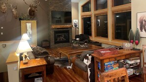 A cozy living room with a fireplace, leather sofas, and a bookshelf filled with board games.
