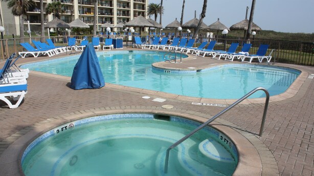 A swimming pool with lounge chairs and umbrellas, surrounded by a brick deck.