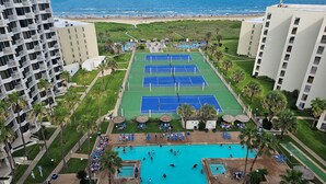 A hotel with multiple tennis courts, a swimming pool, and a beach view.