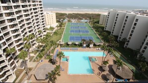 A high-rise hotel with a rooftop pool, tennis courts, and a beach view.