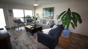 A living room with a sofa, armchair, coffee table, and a large plant.