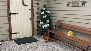 Un banc en bois agrémenté d’un coussin décoratif, un petit sapin de Noël et une pancarte de bienvenue sur la façade d’une maison.