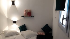 Une chambre à coucher avec un lit, des oreillers, une étagère fixée au mur ornée d’un objet décoratif et une fenêtre donnant sur un paysage.