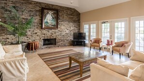 A spacious living room with a stone fireplace, comfortable seating, and large windows.