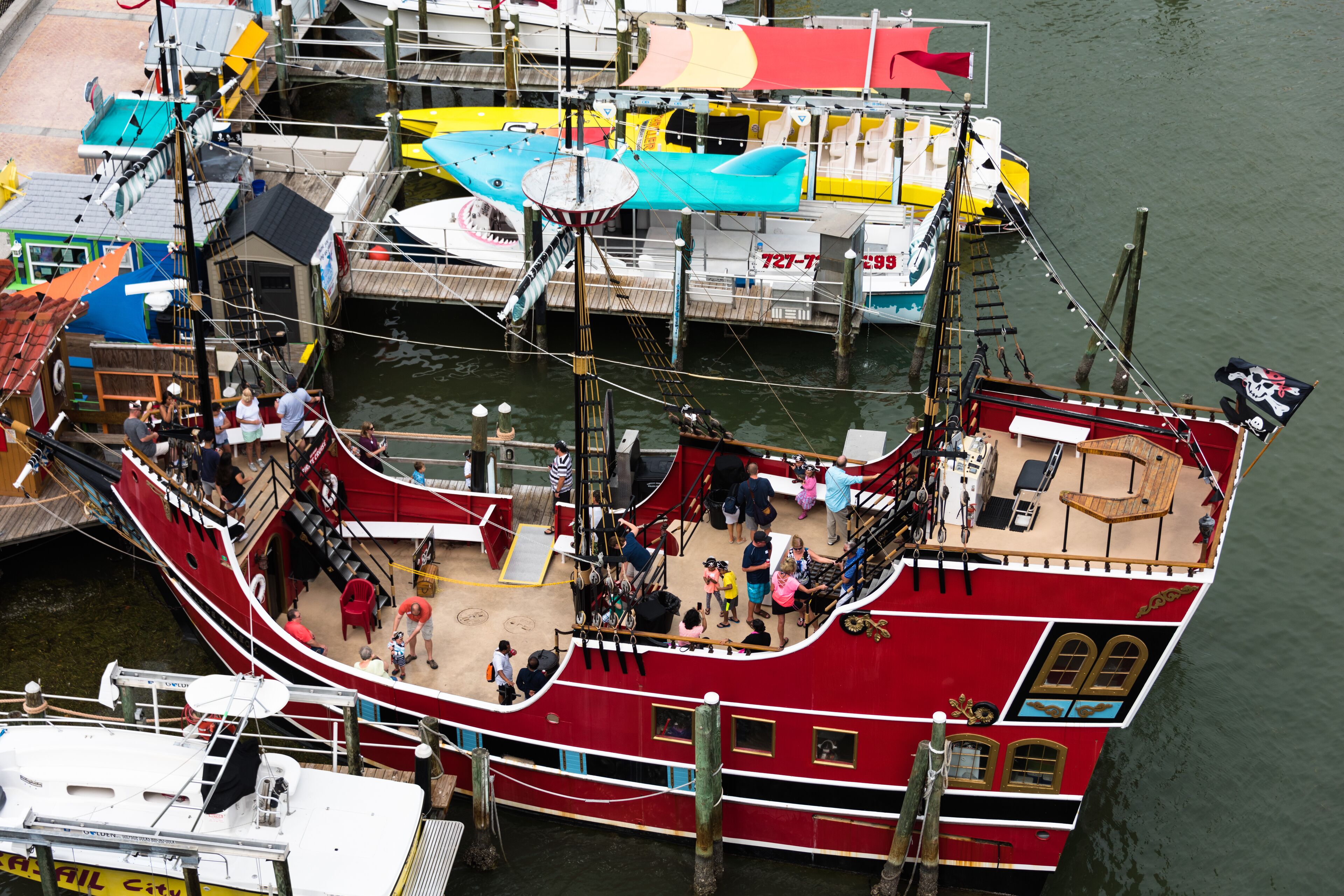 A large red ship docked at a pier with multiple levels, including a deck area and a cabin section.