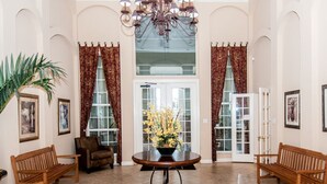 A spacious lobby with a round table, two wooden benches, a potted plant, and a chandelier.