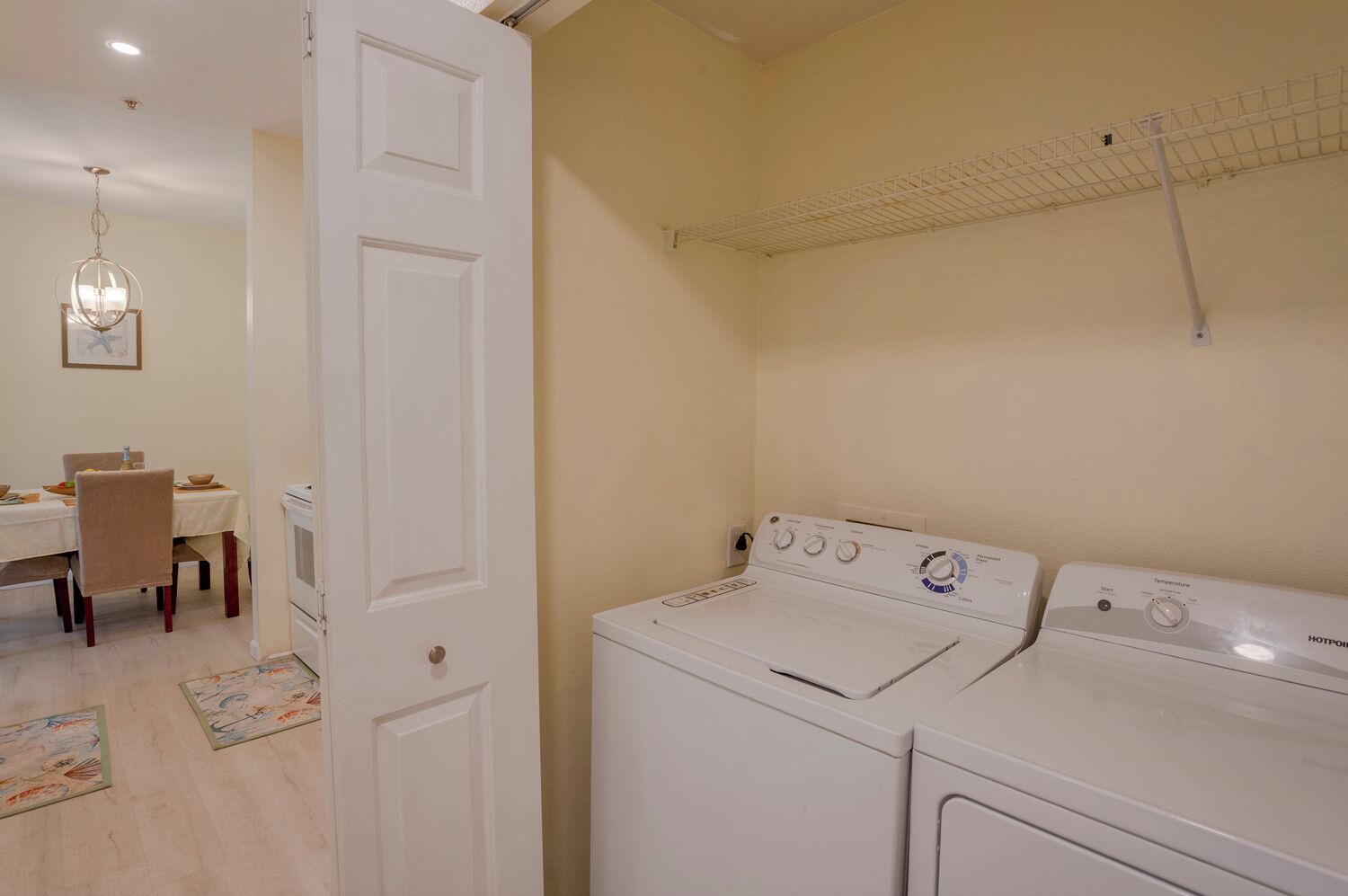 Een wasserette met twee witte wasmachines, een droogrek aan het plafond, een eethoek met een tafel en stoelen, en een kroonluchter.