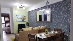 Ein Essbereich mit Holztisch und -stühlen, einer Couch mit gemusterten Kissen, einer kleinen Topfpflanze und einem Wandspiegel.