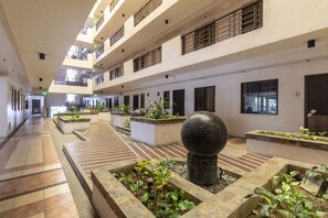 A multi-level indoor courtyard with tiled floors, planters with greenery, and a large spherical sculpture. - Staycation Redwoods Condominuim (Quezon City)