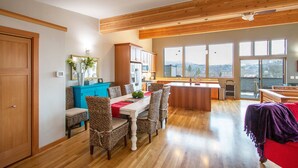 A spacious kitchen with wooden beams, a dining area with wicker chairs, and large windows offering a view. - Blackberry Bramble 3 Bedroom Home by RedAwning (Hood River)