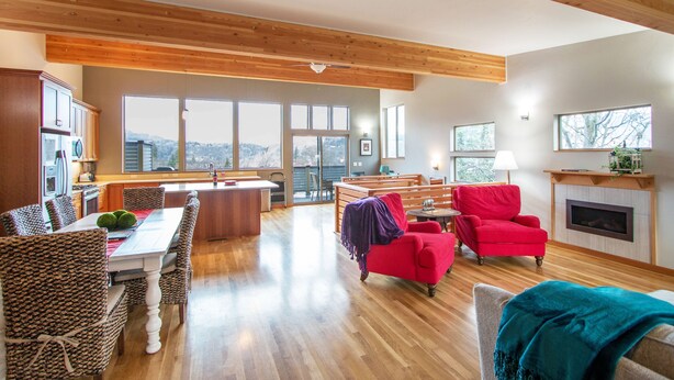A spacious living area with a wooden ceiling, a dining table with wicker chairs, a red armchair, and a fireplace. - Blackberry Bramble 3 Bedroom Home by RedAwning (Hood River)
