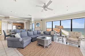 A spacious living area with a large gray sectional sofa, a coffee table, and a view of the ocean.