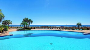 A clear blue pool with a curved edge, surrounded by palm trees and lounge chairs, with a beach and ocean in the background. - SeaChase 1601W by Liquid Life (Orange Beach)