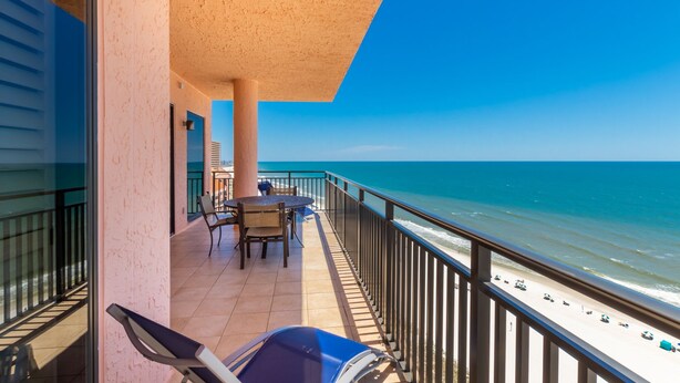 A balcony with a view of the ocean, a table with chairs, and a grill. - SeaChase 1601W by Liquid Life (Orange Beach)